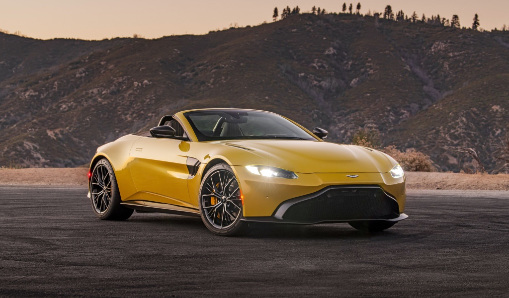 Желтый автомобиль  Aston Martin Vantage Roadster, 2021 года на фоне холмов