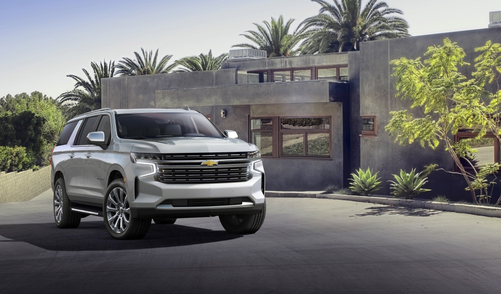 Серый внедорожник Chevrolet Suburban, 2021 года на фоне дома