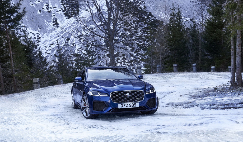Синий автомобиль Jaguar XF зимой на фоне горы 