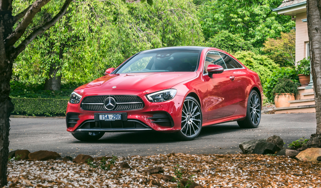 Красный автомобиль Mercedes-Benz E 300 AMG, 2020 года у дома осенью