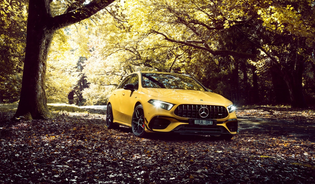 Желтый автомобиль Mercedes-AMG A 45 S,  2020 года в осеннем лесу 