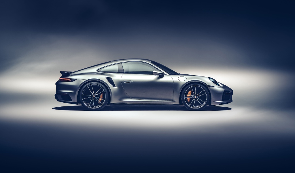 Серебристый автомобиль Porsche 911 Turbo S 2020 года вид сбоку на сером фоне