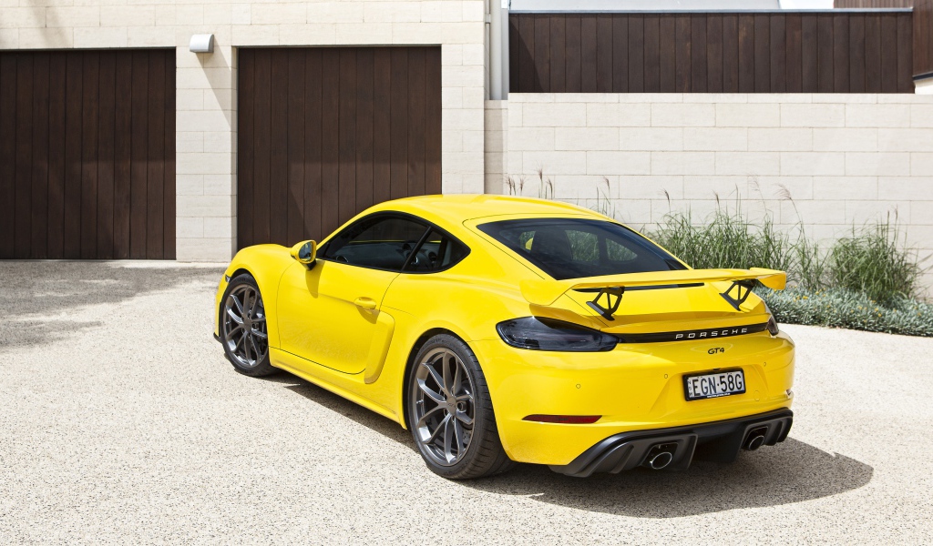 Желтый автомобиль Porsche 718 Cayman GT4, 2020 года у гаража 