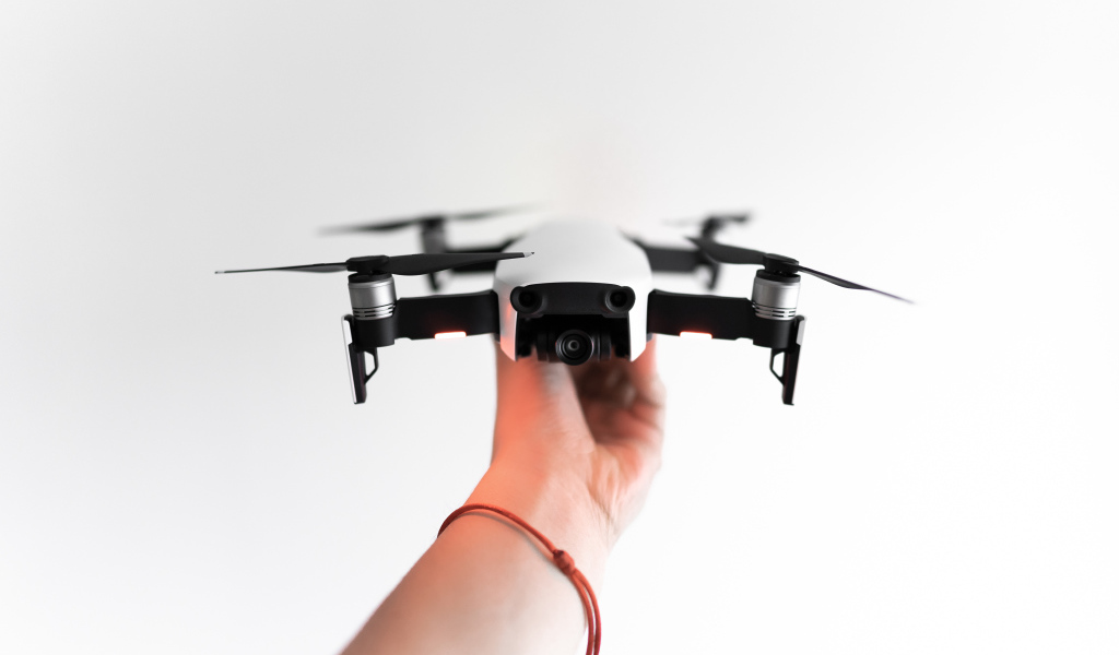 Белый квадрокоптер в руке на белом фоне