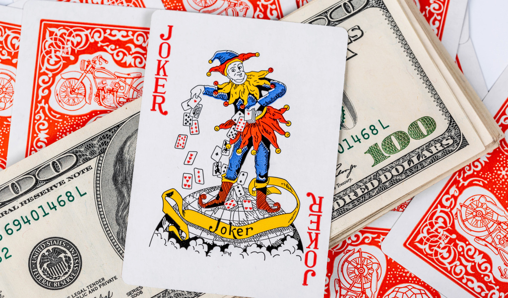 Карточный Джокер и пачка стодолларовых купюр