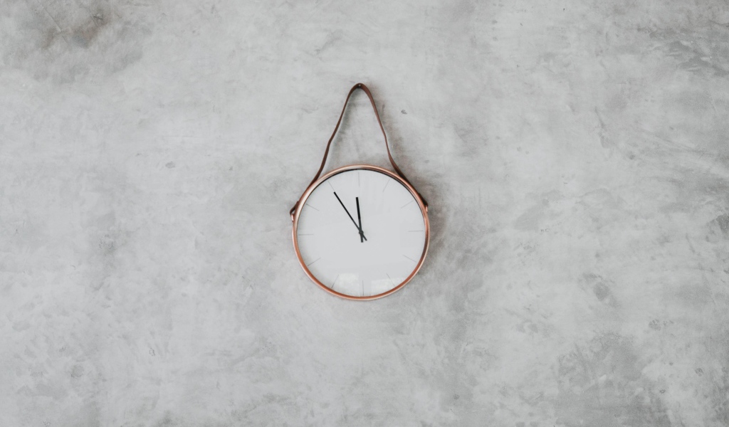 Часы с черными стрелками висят на серой стене 