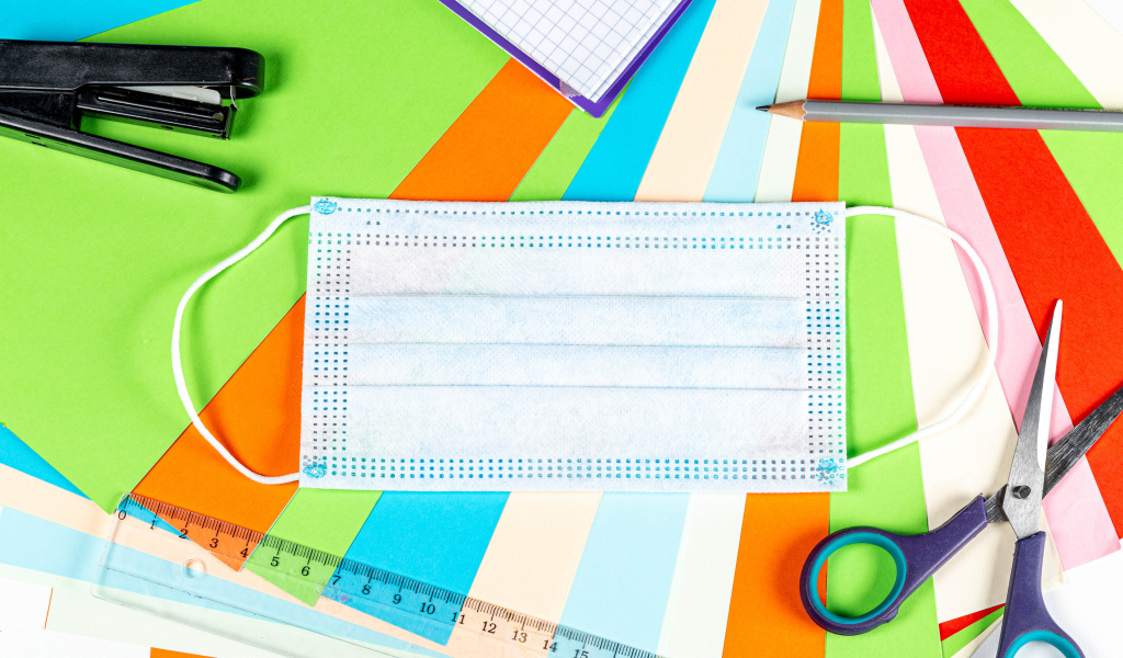 Маска от коронавируса лежит на цветной бумаге с канцелярскими предметами