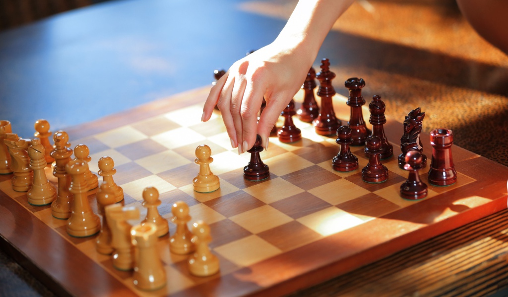 Женская рука переставляет шахматы на доске 