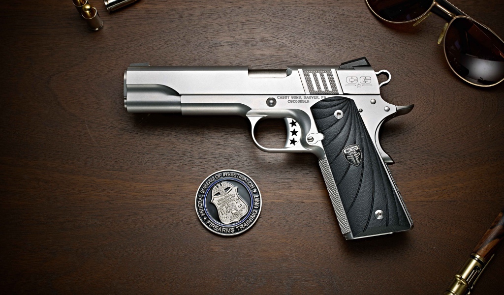 Пистолет Cabot 1911 лежит на столе с очками и жетоном 