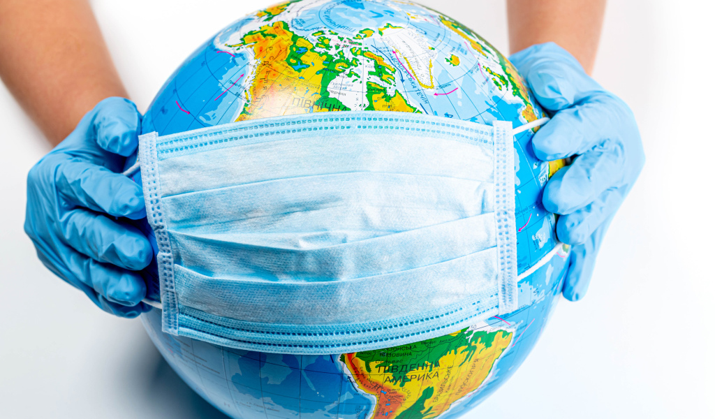 Руки одевают маску от коронавируса на глобус 