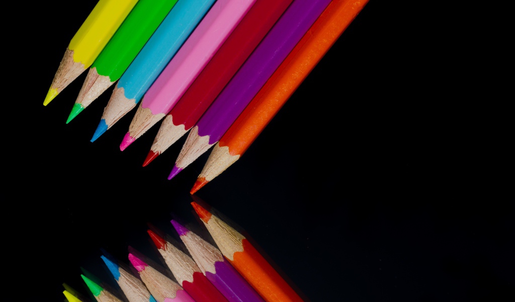Разноцветные карандаши отражаются в черной зеркальной поверхности 