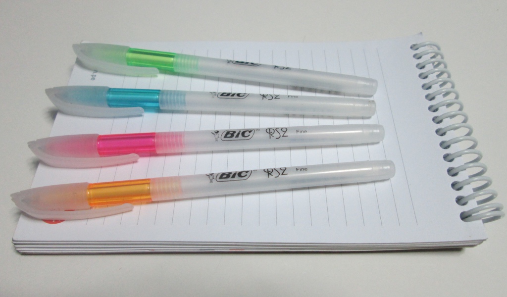 Разноцветные ручки лежат на блокноте на белом фоне 