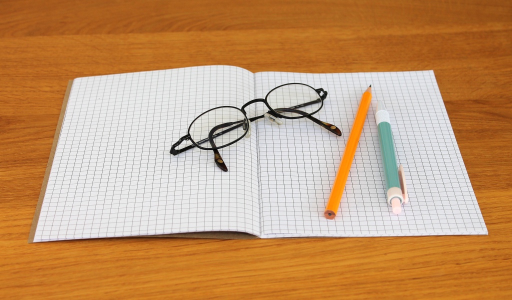 Тетрадь, ручка, карандаш и очки лежат на парте