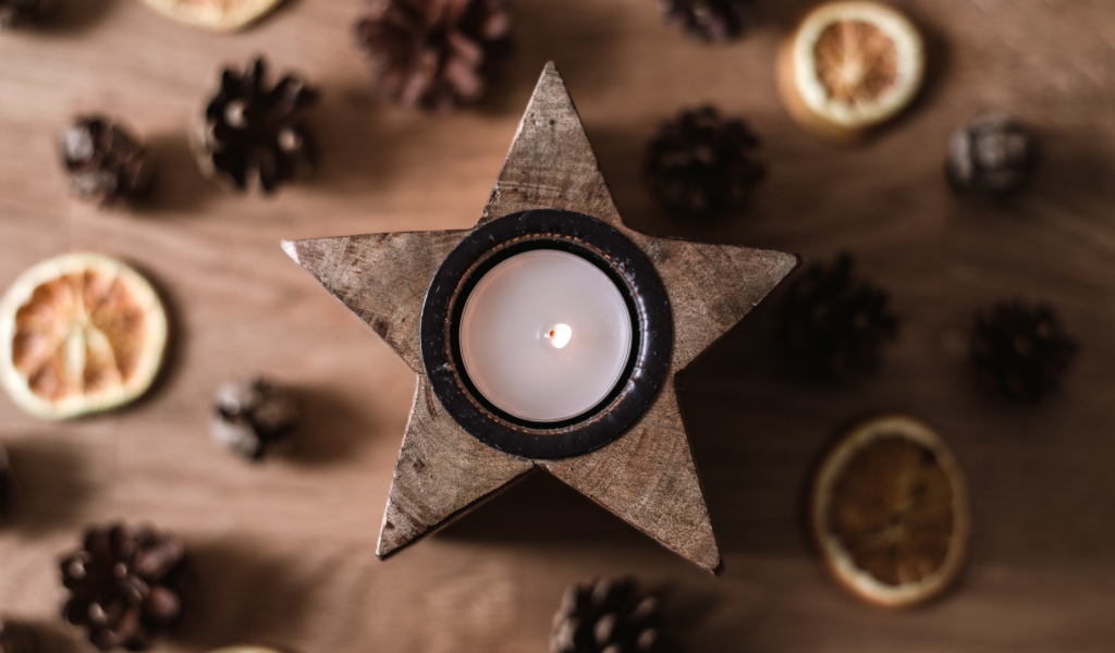 Star shaped candle on table with pine cones and dried orange
