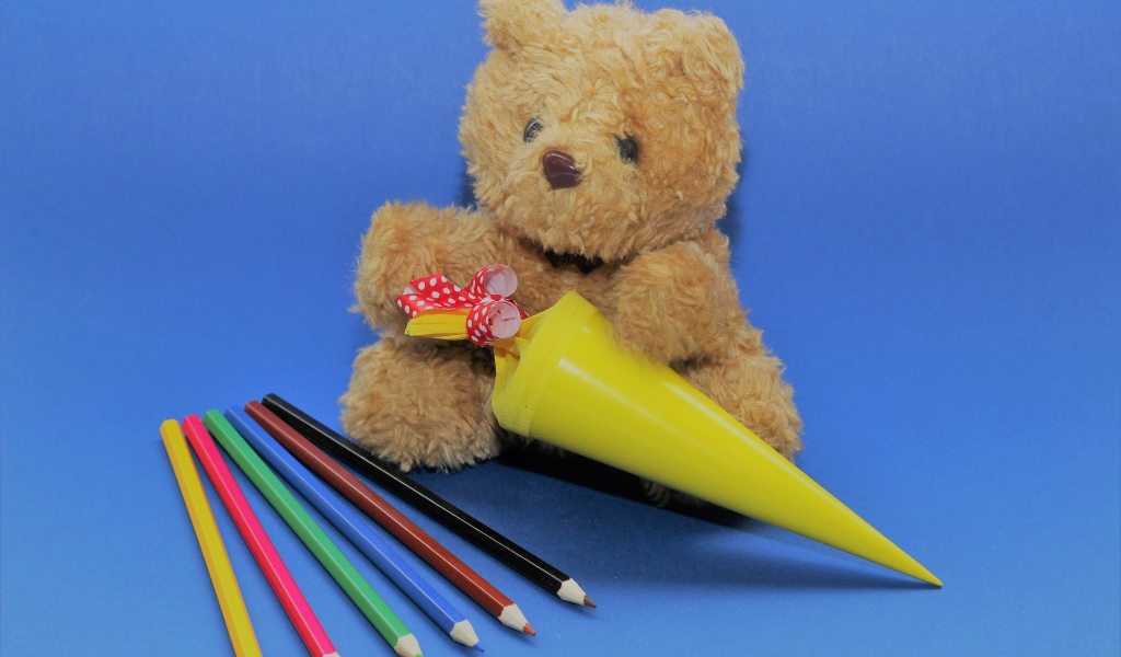Игрушечный медвежонок  с карандашами на синем фоне