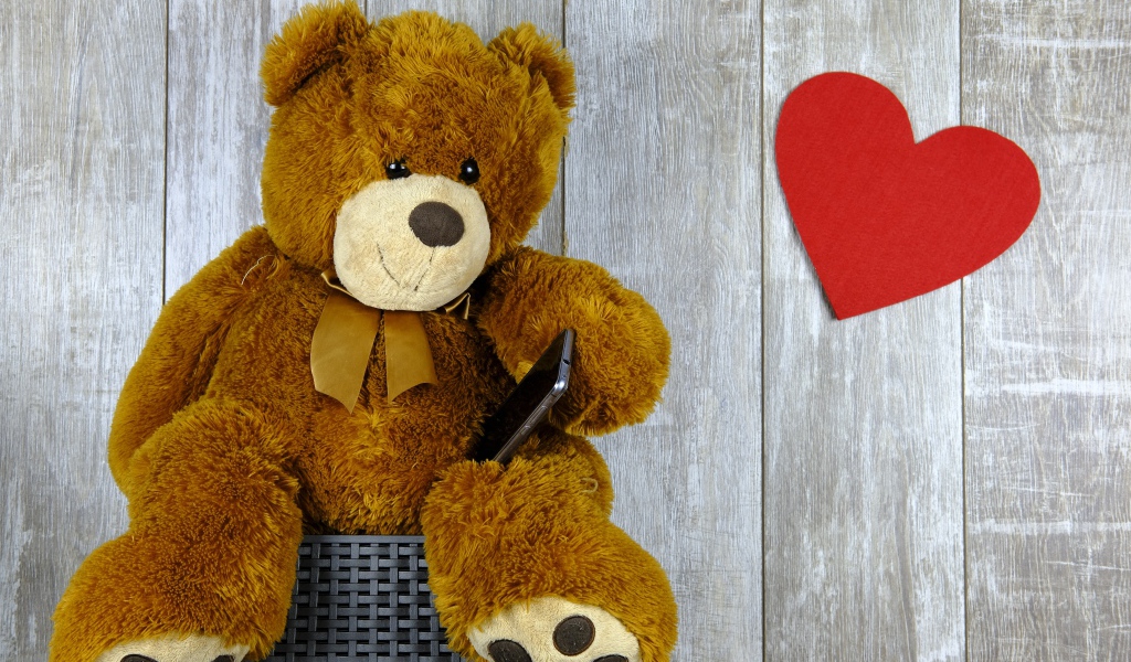 Плюшевый медведь с красным сердцем на деревянном фоне