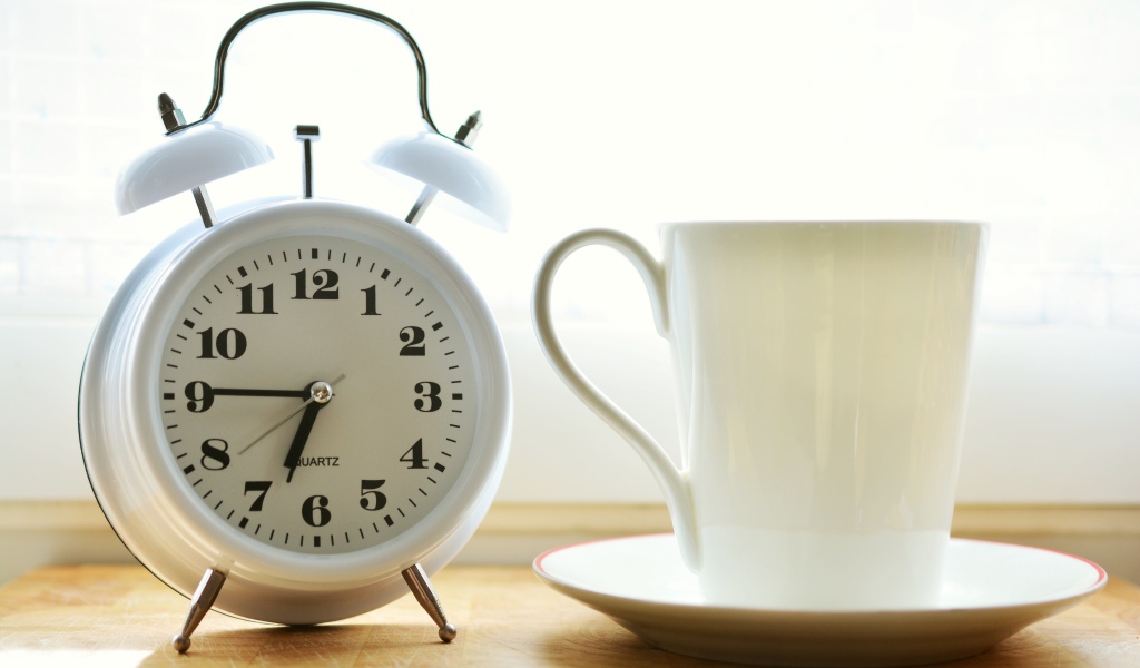 Белый будильник и чашка кофе на утреннем столе