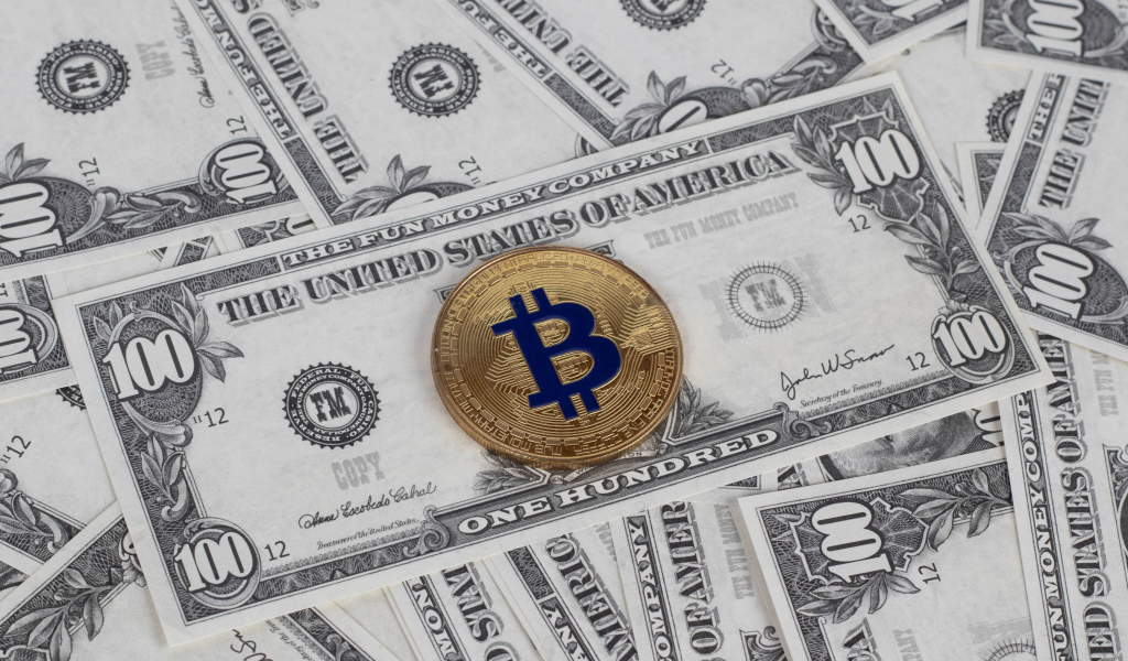 Монета Биткоин лежит на стодолларовых купюрах