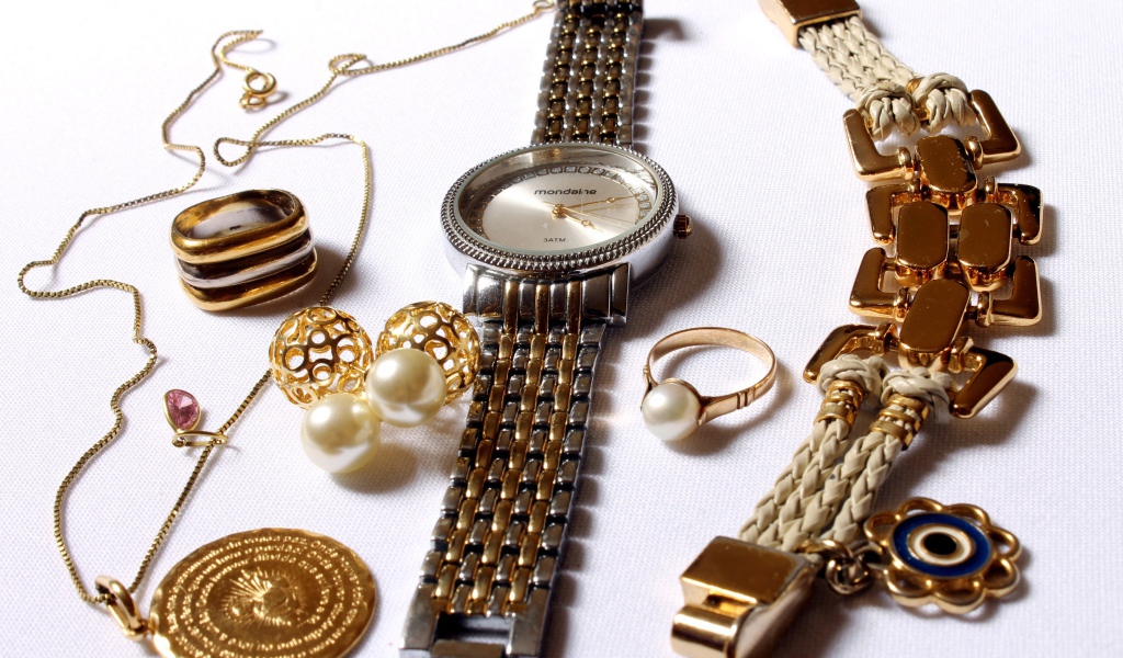 Наручные часы и золотые украшения на белом фоне