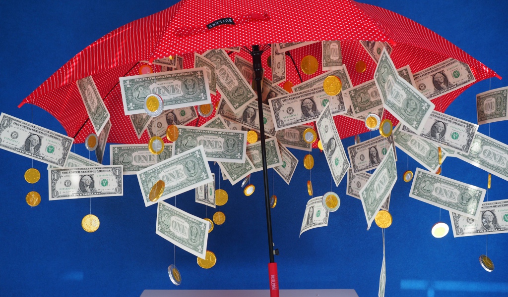 Доллары и монеты высыпаются из зонта на голубом фоне