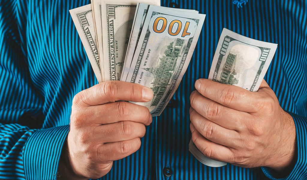 Мужчина считает сто долларовые купюры 