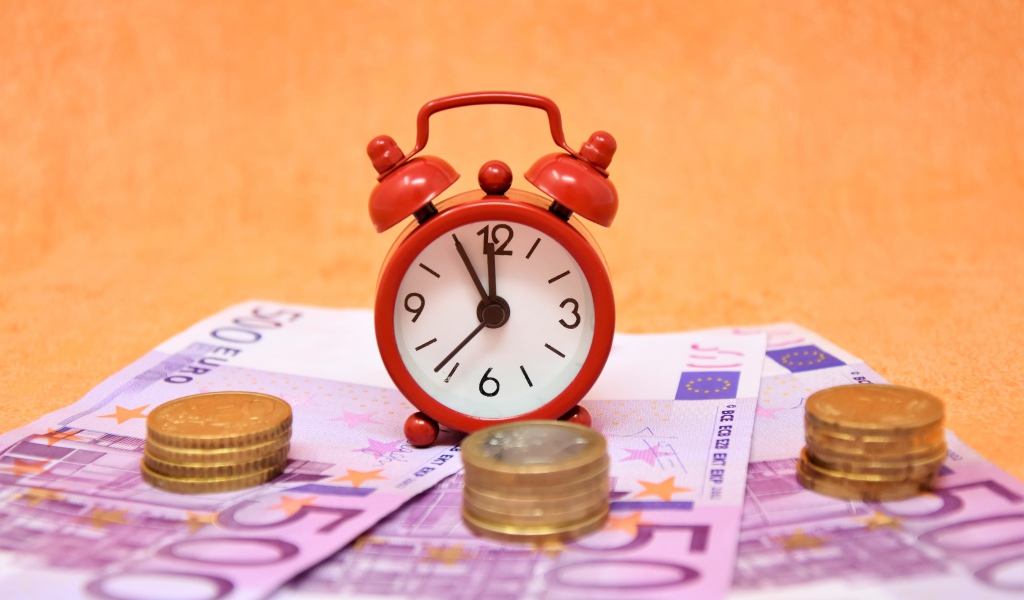 Маленький красный будильник с купюрами евро и монетами