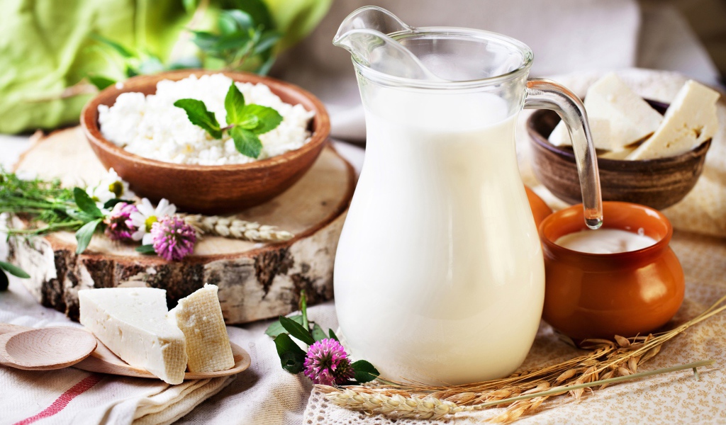 Кувшин с молоком стоит на столе с сыром и творогом