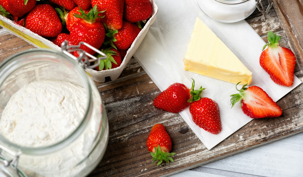 Кусок масла на столе с клубникой и мукой 