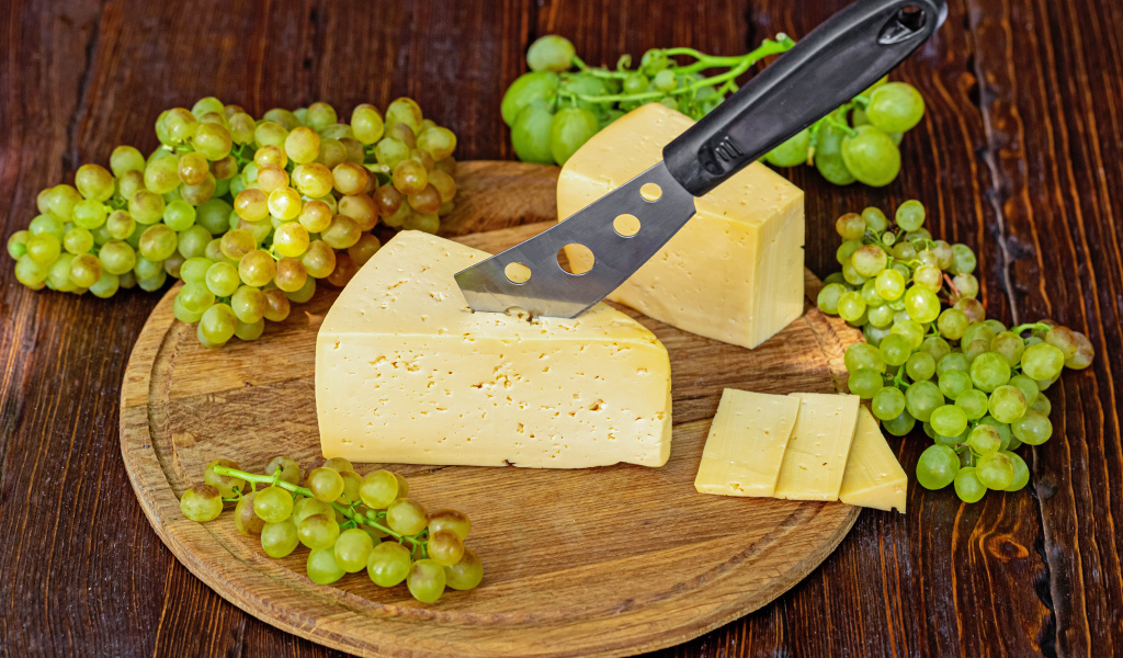 Кусок твердого сыра на столе с ножом и белым виноградом