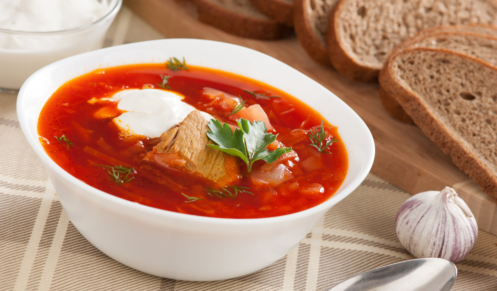 Тарелка горячего борща на столе с хлебом и чесноком