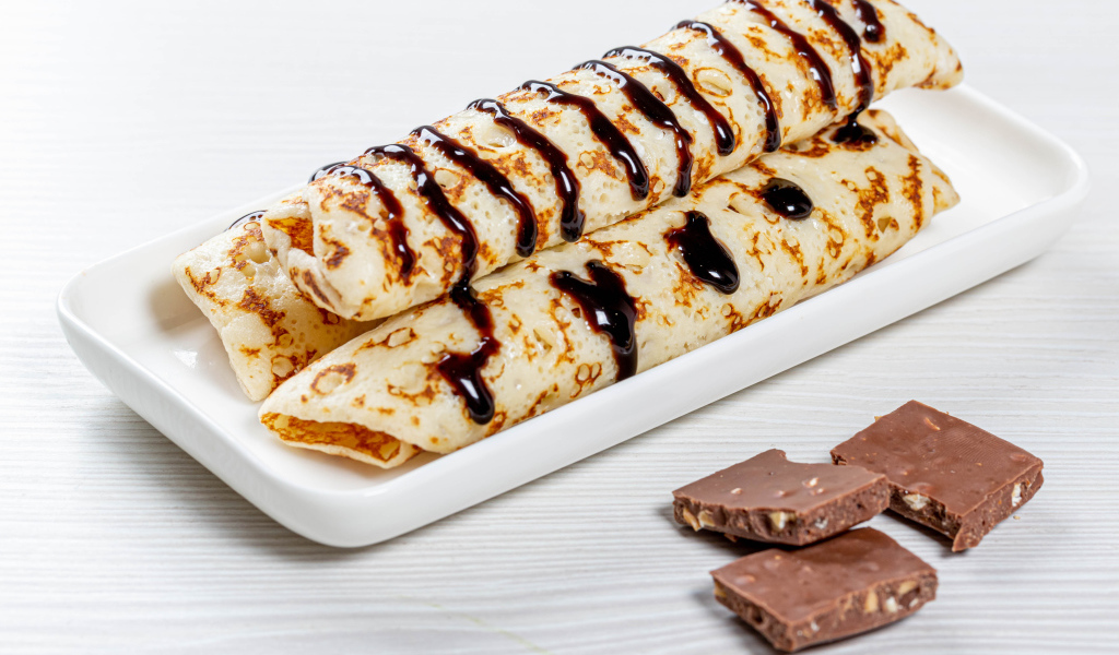 Аппетитные тонкие блины на белой тарелке с шоколадом