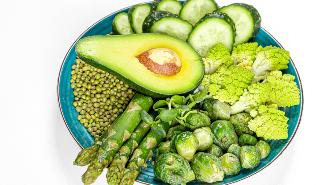 Авокадо, капуста, огурцы и спаржа на тарелке на белом фоне