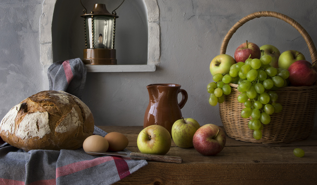 Корзина с яблоками и виноградом на столе с хлебом и яйцами