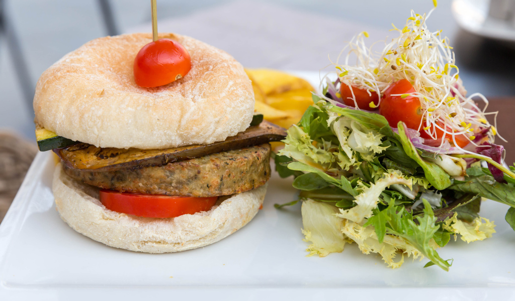 Большой гамбургер с салатом на столе 