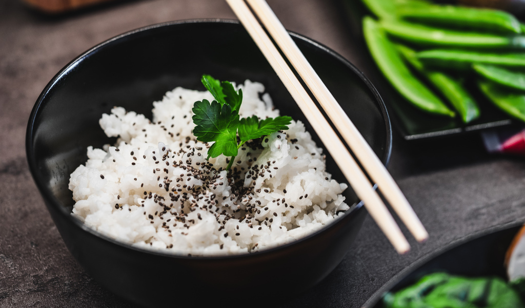 Вареный рис с семенами  в черной миске с палочками