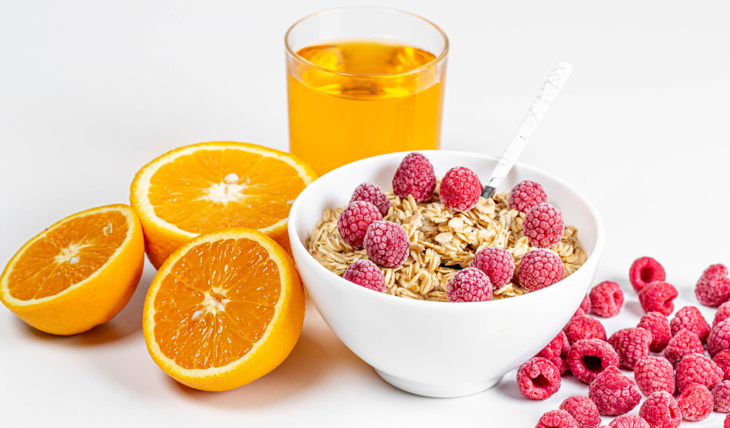 Миска мюсли с ягодами малины и апельсинами на столе с соком