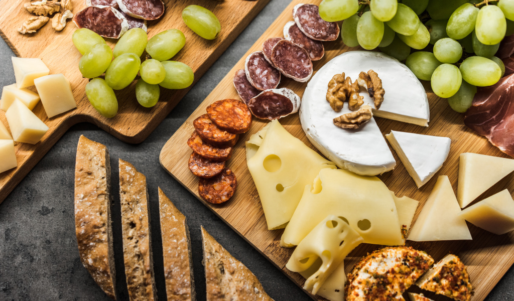 Сыр, колбаса, виноград и батон  на столе 