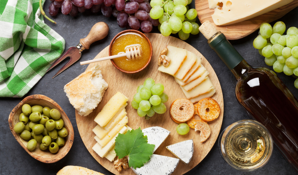 Сыр на столе с виноградом, оливками и белым вином