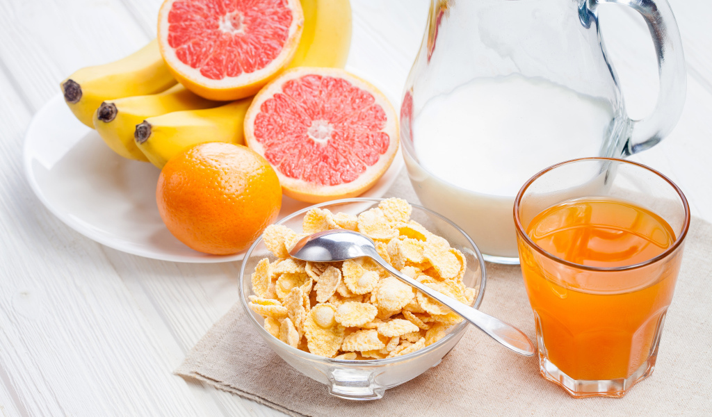 Кукурузные хлопья на столе с молоком, соком и свежими фруктами на завтрак
