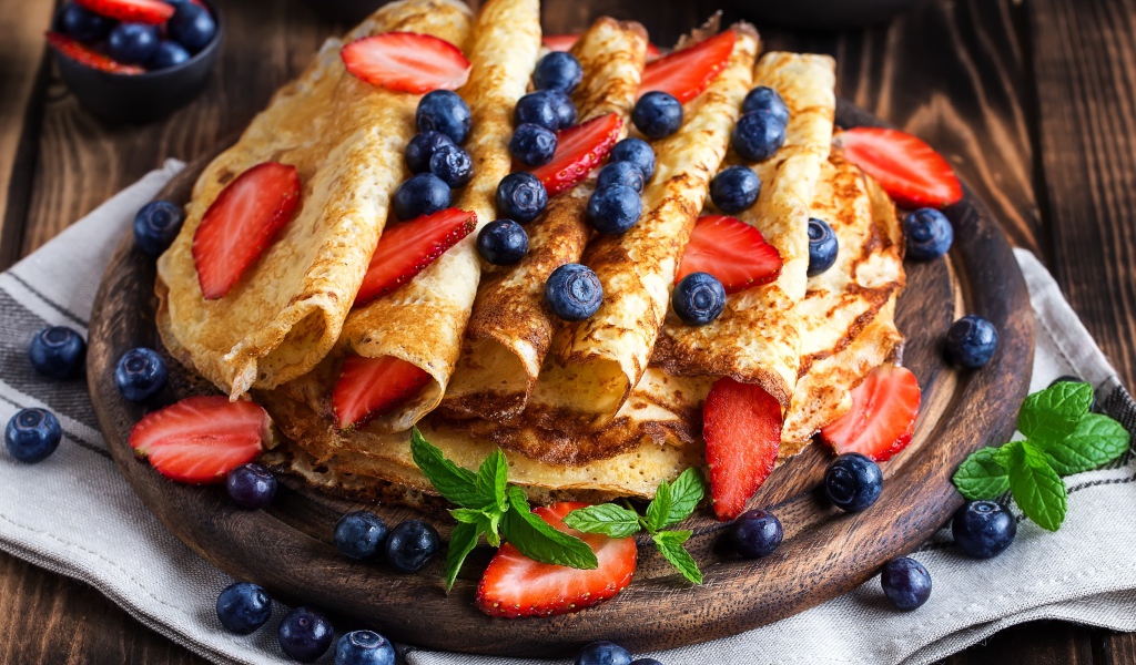 Вкусные тонкие блинчики на деревянной доске с ягодами черники и клубники 