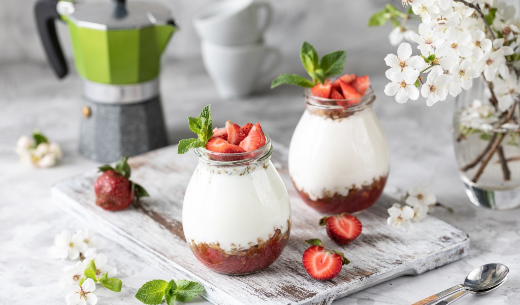 Десерт с йогуртом в банке с клубникой на столе цветами вишни 