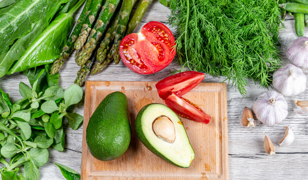 Свежая зелень на столе с авокадо, помидором и чесноком