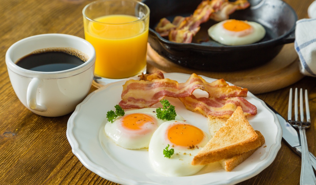 Яичница с беконом и тостами на столе с соком и кофе