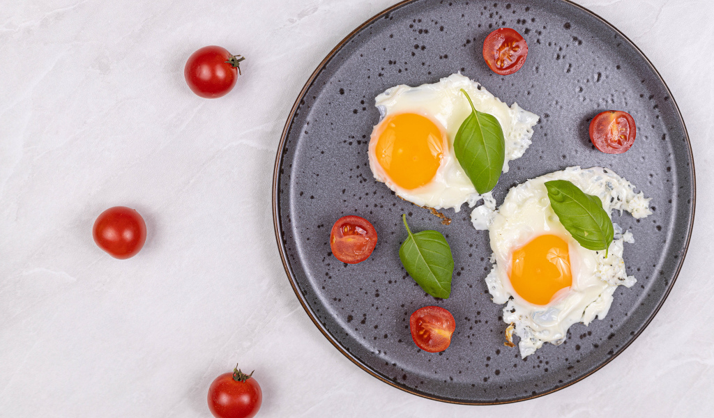 Яичница глазунья с помидорами и листьями базилика на черной тарелке 