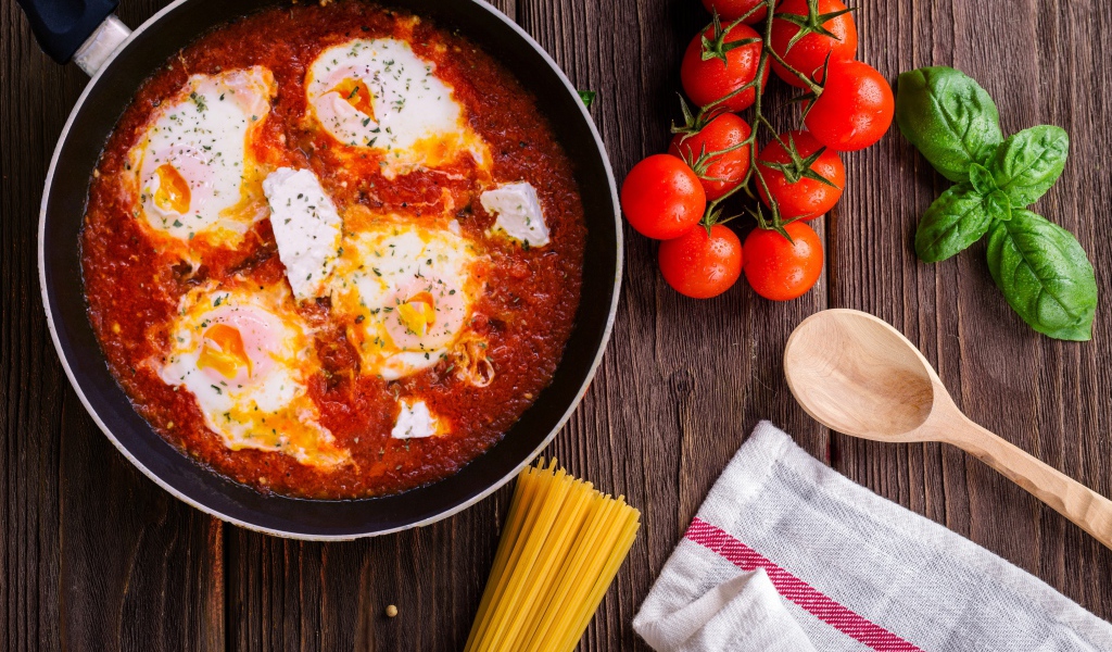 Греческое блюдо с томатами и яйцами на столе с спагетти и помидорами