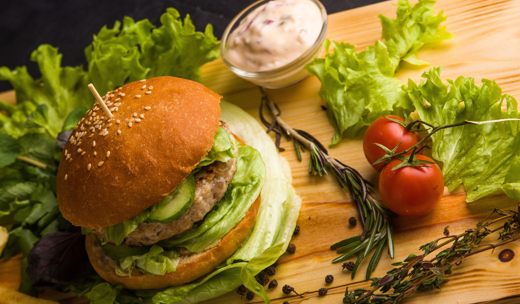 Hamburger on a table with lettuce, spices, tomatoes and sauce