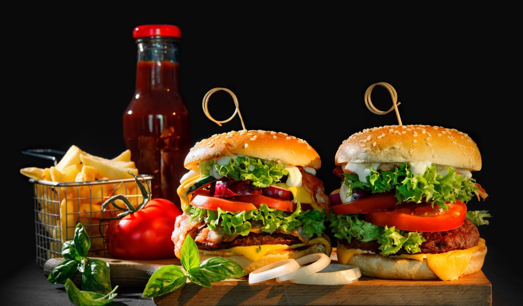 Гамбургеры на столе с картофелем и кетчупом на черном фоне