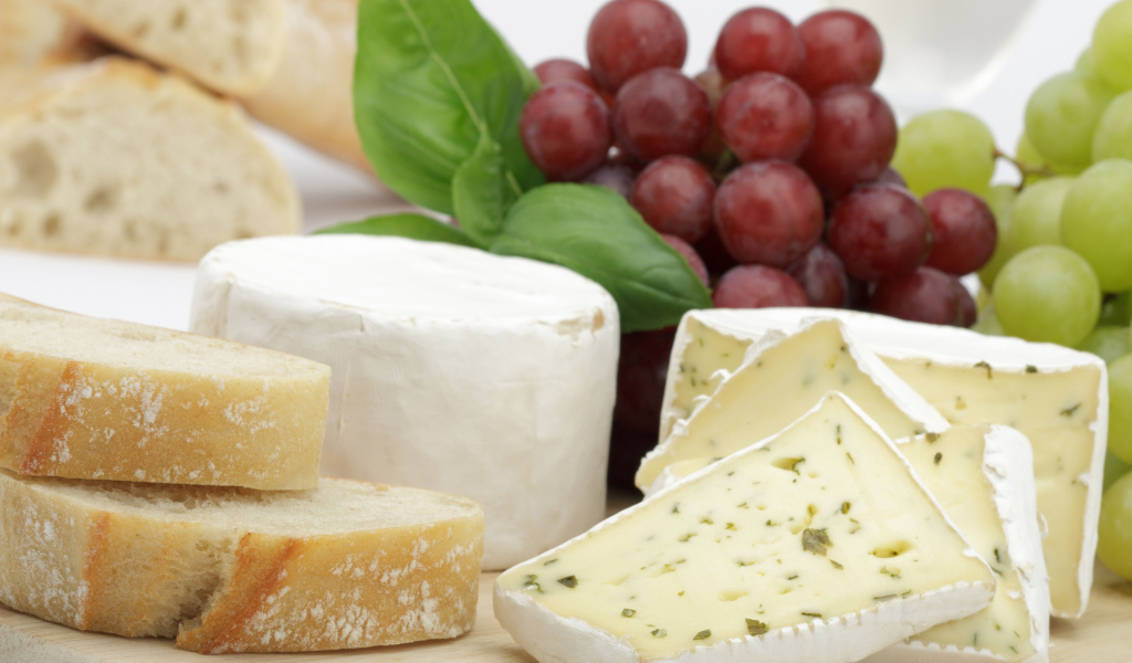 Твердый сыр на столе с батоном и виноградом