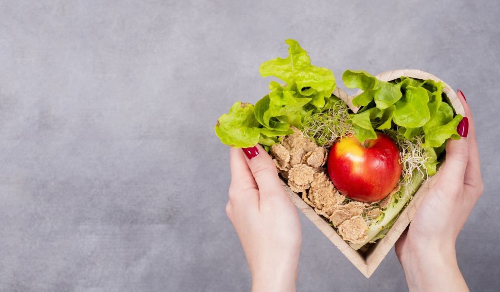 Коробка в форме сердца с яблоком и листьями салата 