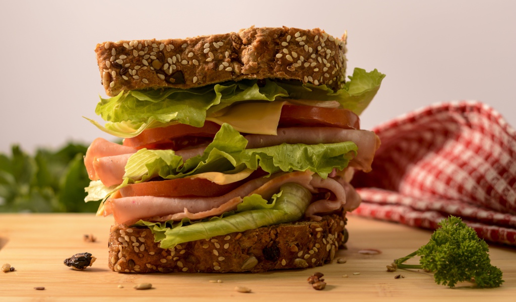 Большой бутерброд с ветчиной, сыром, помидорами и листьями салата 